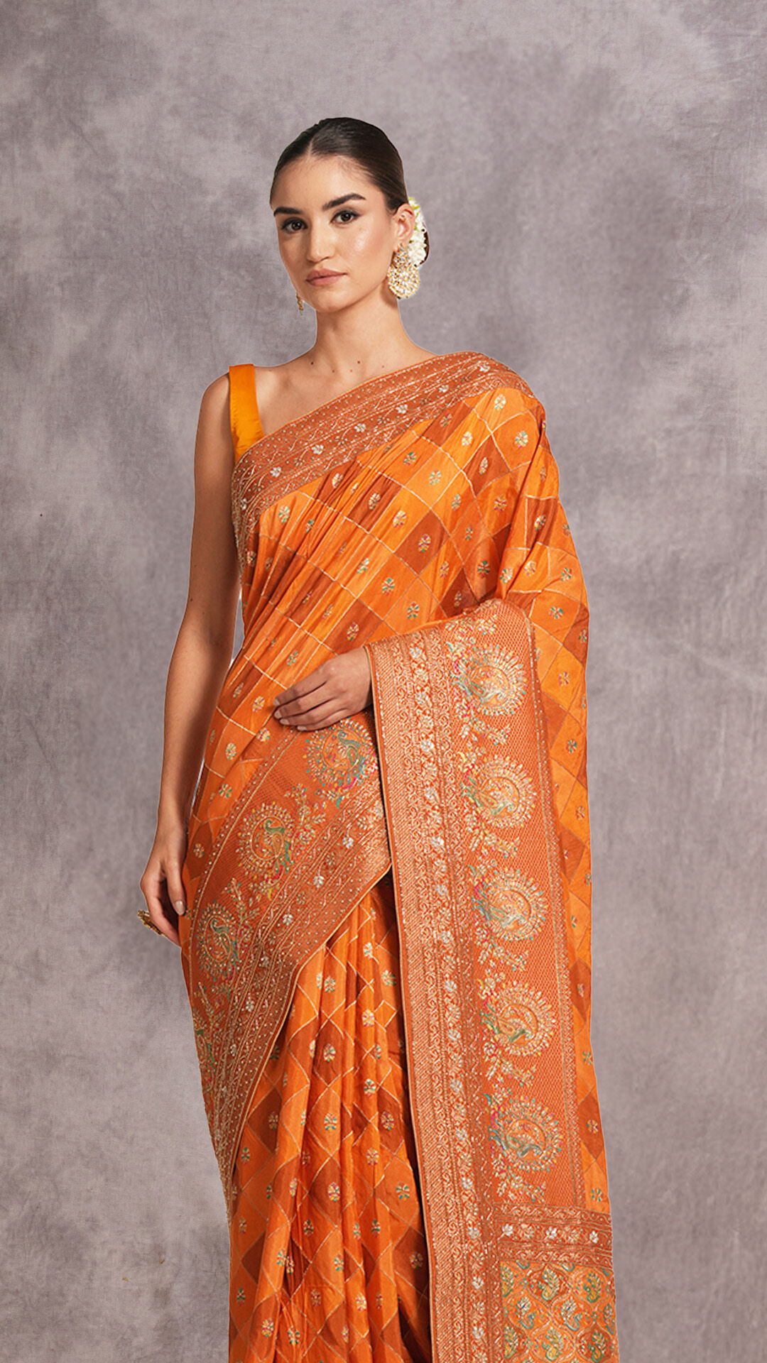 Woman in an orange checkered Banarasi silk saree with an embroidered border and a matching sleeveless blouse.